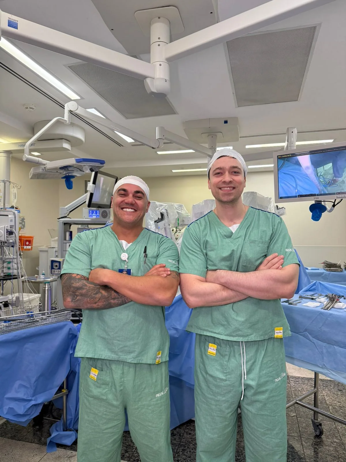 Dr. Allan Morrell ao lado de outro cirurgião em sala de cirurgia robótica
